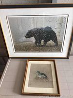 Photo showing two framed art prints by Gordon Pynn; bear print in dark frame above, bird print in lighter frame below