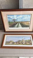 Two framed landscape art prints stacked vertically, showing rural scenes with wood-finish frames.
