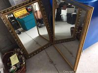 Two of the ornate gold framed mirrors standing on the floor showing reflections and frame details.