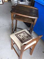 Full view of vintage children's wooden desk and upholstered chair showing worn wood surface and chair seat pattern.