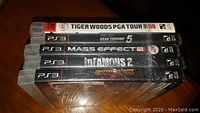 Stack of five PS3 game spines: Tiger Woods PGA Tour 08, Gran Turismo 5, Mass Effect 2, inFAMOUS 2, MotorStorm