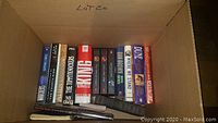 Box with novels and fiction books, many hardcovers with visible titles including Stephen King and Dune
