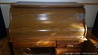 Closed view of wood roll top desk showing curved slat roll top and base drawers with carved handles.