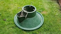 Photo of the green Christmas tree stand showing the wide circular base, water reservoir, and metal gripping screws.