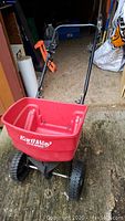 Red EarthWay seed and fertilizer spreader with large black wheels and handle.