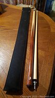 Two-piece Dufferin pool cue laid on table next to black soft carrying case, showing full length and condition
