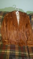 Full front view of brown lady's fur jacket on hanger, showing texture, collar, and button details