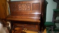 Front view of the antique upright piano showing upper carved panel and wood grain finish