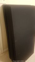 Four black acoustic panels stacked together against a wall. Panels are rectangular with dimensions approximately 25.5 x 49.5 x 2.5 inches. Covered in black fabric with a smooth appearance, showing some surface marks but structurally intact.