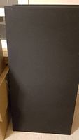 Photo shows a close-up view of one black acoustic panel standing upright, rectangular with dimensions roughly 25.5 x 49.5 inches and thickness 2.5 inches, covered in smooth black fabric.