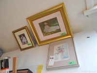 Three framed art prints positioned against a wall. Visible are a Monet-style print, clown print, and floral print.
