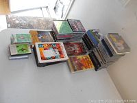 Photo showing multiple stacks of CDs, DVDs, VHS tapes and audio cassettes arranged on a white table.