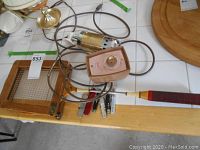 Photo showing the wooden badminton racket, the vintage Niagara hand massager with electrical cord and control box, and five of the six pocket knives with various handles laid out.