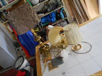 Photo showing three lamps: two table lamps with patterned and pleated fabric shades, and one wall mounted brass lamp with bracket and no shade.