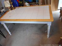 Full view of rectangular wood framed dining table with white tile top, shows turned white legs and natural wood border.
