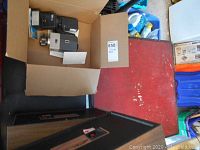 Cardboard box containing the camera and flash modules shown at an angle, atop part of the folding card table.