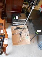 Silver microphone stand placed on cardboard box among other items, showing stand condition and included accessories.