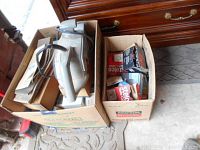 Two worn electric belt sanders inside cardboard boxes with cords wrapped around and sanding belts visible.