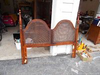 Full view of the queen size wooden headboard showing double arched cane panels and the posts with finials on either side.