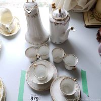 Photo of chocolate pot with 6 demitasse cups and saucers, gravy bowl and plate, all in Limoges Old Abbey pattern with gold trim showing wear and one chipped cup.