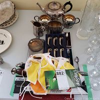 Overview of silver plate tea set with teapot, creamer, sugar bowl, place cards, bottle stoppers, and boxed cutlery sets