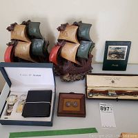 Overview of lot showing porcelain bookends, Cote d’Azur box with watch, wallet, keychain, framed coins, Travelog book, jewelry watch box