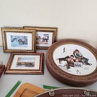 Overview of three small framed prints and two round framed Norman Rockwell plates on a flat surface
