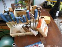 Overview of all tools in plastic caddy with screwdrivers, tool box, boxes, and assorted small tools on table