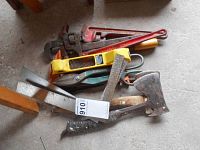 Photo showing a collection of tools including 2 vintage wooden-handled hatchets, several pipe wrenches including a large red one, a yellow-handled saw or cutter, and a black-handled tool