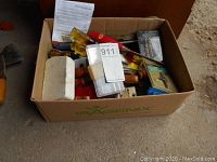 Full box containing assorted hand tools and accessories, showing wooden handles and some packaged drill bits.