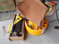 Photo showing stacked sandpaper sheets on top of the yellow plastic tool caddy filled with screwdrivers and visible handles of various tools.