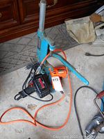 Wide view of the three items showing the blue drill press, a black Craftsman drill, and an orange B&D drill with power cords tangled.