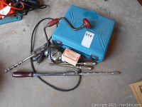 Full view of Makita drill case, hand brace with auger bit, Stanley Yankee driver, two hole drivers, drill chuck, and Skil electric drill parts on concrete floor.