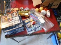 Photo of various home repair items arranged on red table including storm window kits in boxes, brass valve, packaged timers, door knobs, and toilet repair parts.