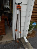 Three pipe clamps showing full length, leaning against white wall, visible rust and wear