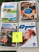 Four Nintendo Wii game cases: Wii Sports Resort, Wii American Idol Season 2, Wii Classic British Motor Racing, and Wii GT Pro Series, arranged on a surface with a yellow sticky note.