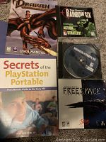 Five PC video game-related items laid out: Drakan manual, Rainbow Six game case, Soldier of Fortune disc, Secrets of PSP book, Descent Freespace game case.