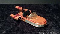 Angled side front view of vintage orange Star Wars Land Speeder toy, showing cockpit area and three engine pods.