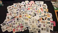Large collection of assorted mostly canceled postage stamps on torn paper pieces spread on a flat surface.