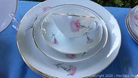 Close-up of tea cup nested in a soup bowl and dinner plate showing pink carnation flower and gold rim detail.