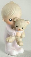 Porcelain figurine of a child in light-colored pajamas hugging a teddy bear with big black eyes