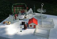Full view of lot items on outdoor table including crystal Santa candle holder, nativity set figures, model houses, fences, oven mitts, and petit four plate.