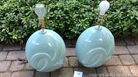 Pair of celadon green lamps with smooth oval bodies and decorative embossed swirls, outdoor setting.