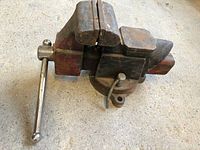 Metal antique bench vise showing jaws, handle, and rotating base from above.