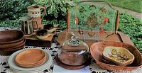 Wide view of entire lot displayed on crochet tablecloth outside with garden background showing teak bowls, plates, cheese board, glass tray, and pottery mugs.