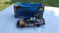 Side view of the 1/24 NASCAR Jeff Gordon Dupont Flame model car alongside its original blue display box labeled Jeff Gordon 24.
