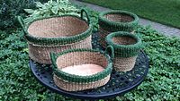 All four woven baskets on an outdoor metal table with a grassy background.