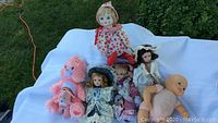 Photo of all dolls including the baby doll, three porcelain head dolls, pink Care Bear, and plastic baby doll on white background outside
