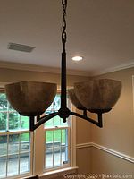 Hanging light fixture with amber glass shades suspended from ceiling chain, shown lit or unlit in room interior.