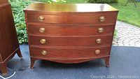Front view of vintage mahogany dresser with four curved drawers and oval brass handles.